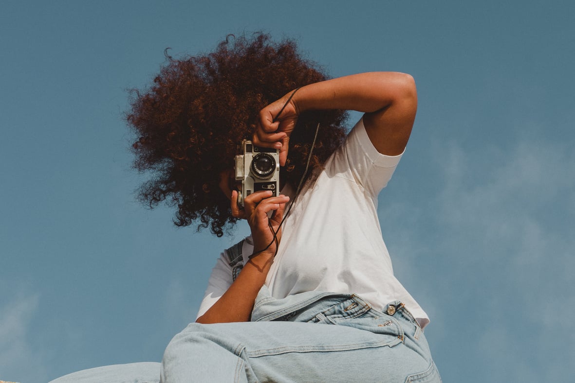 Woman Taking a Picture with Vintage Camera against the Sky